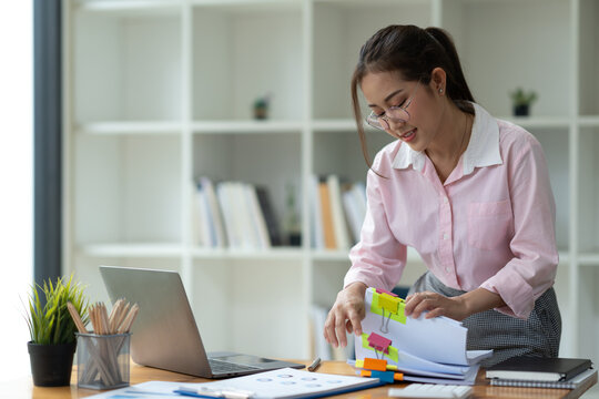 Asian Businesswoman Working In Piles Of Paper Files Documents In The Meeting To Search And Review The Various Work Folders At The Desk To Record Information. Management Concept