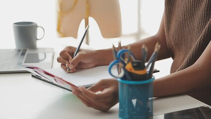 Caucasian female fashion designer works in studio by idea drawing sketches with digital tablet and colorful fabric for a dress design collection, choose clothing colors for tailoring and designing