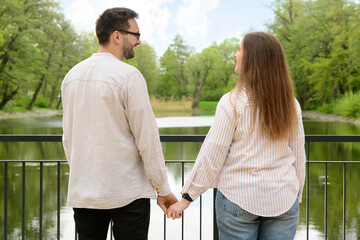 Beautiful loving happy couple holding hands on bridge in park