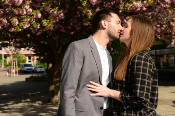 Beautiful loving young couple kissing near blooming tree on sunny spring day
