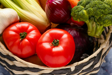 Wicker bowl with different fresh vegetables on blue background, closeup