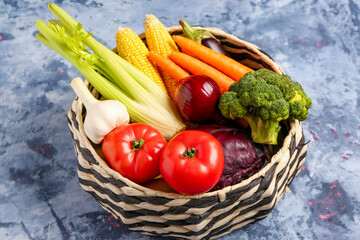 Wicker bowl with different fresh vegetables on blue background