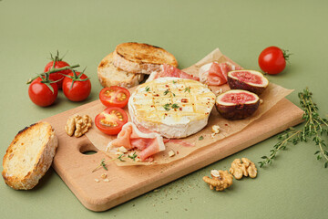 Wooden board with tasty baked Camembert cheese on green background