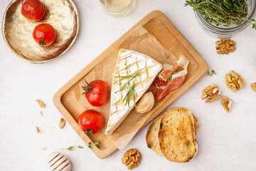 Wooden board with tasty baked Camembert cheese on light background