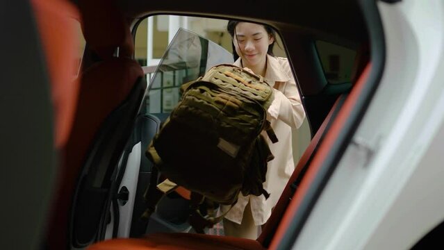 Happy young asian woman tourist opening car door and putting his backpack suitcase package luggage on rear seat, Loading a car for a roadtrip, Travel. Summer adventure