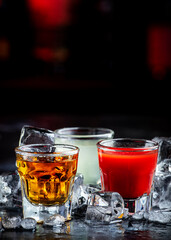 Golden tequila with sangrita and lime juice. Black bar counter background, steel bar tools and bottles