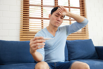 young man have a high fever from checking a digital thermometer measure body temperature at home