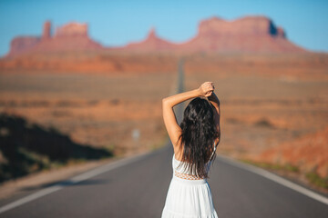 Happy young woman in white dress on the famous road to Monument Valley in Utah. Amazing view of the...