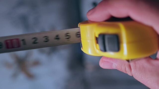 Foreman using yellow tape measure, close up. Person taking measurements using tape line for a room renovation.