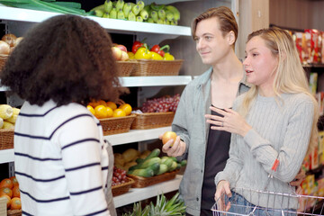 Happy cheerful caucasian young couple with a shopping basket talking with female shopkeeper.