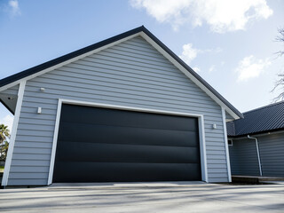 Double gray garage with black tilt-up retractable raised panel metal door and gable metal roof - obrazy, fototapety, plakaty