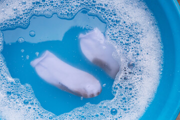 Dirty white socks soaked in water, dissolving detergent in blue basin.
