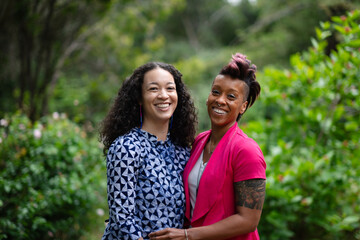 A cheerful, joyful lesbian couple stands face to face in an affectionate embrace. Their happiness...