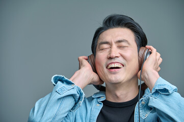Middle-aged man sitting in a chair, wearing a headset and listening to music on his smartphone