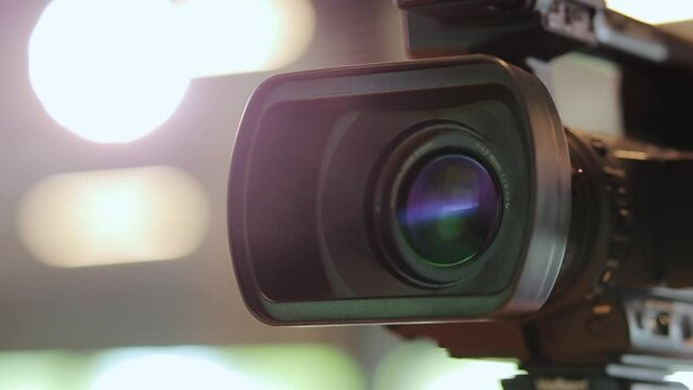 Professional video camera. Camera lens, bokeh background. Professional equipment for the production of video content. Shooting a news report. Journalism. Focusing lens of a video camera. 