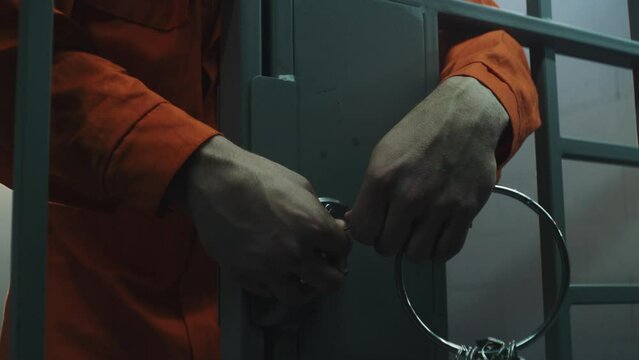 Male prisoner steals keys and opens prison cell through metal bars. Criminal in orange uniform escapes from jail. Inmate, thief serves term in detention center or correctional facility. Close up.