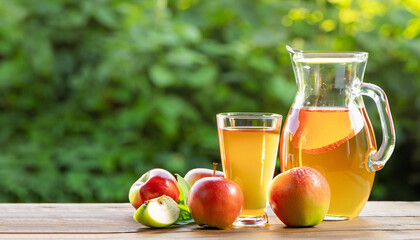cider or juice in glass decanter with ripe fresh apples on wooden table with green natural background. Copy space. Summer drink