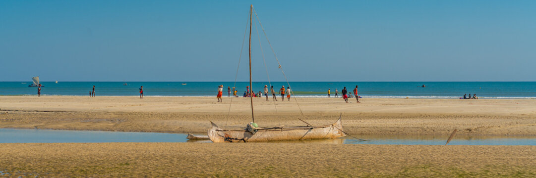 Coastline from Morondava with a baobab wood boat at low tide on sand, background with people panorama