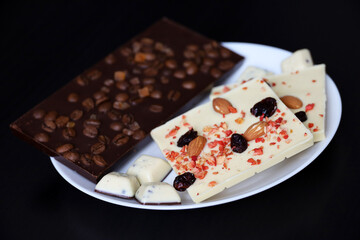 White and dark chocolate with dried raisins, coffee beans and nuts. Tasty dessert in plate on dark wooden table