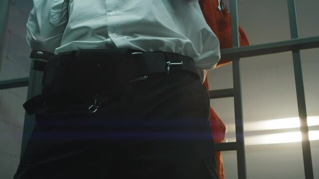 Male prisoner kills jailer through metal bars, takes keys and opens prison cell. Criminal in orange uniform escapes from jail. Serving term in detention center or correctional facility. Close up.