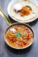 Traditional Sev bhaji or sev tamatar nu Shaak with Jowar Bhakri. Sev is a crisp fried gram flour vermicelli. Served with chopped onion and lemon. with Copy space. Its a sweet and spicy indian curry.