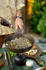 Man frying onion with greens on a pan, cooking some healthy food in garden outdoors, close-up