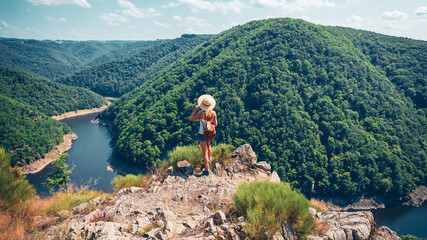 Woman with hat and backpack standing on mountain peak enjoying beautiful view (Dordogne in France)-...
