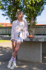 Portrait of a modern girl in short shorts. stands near the tennis table, holds table tennis rackets in his hands. Laughs merrily. Outdoors.