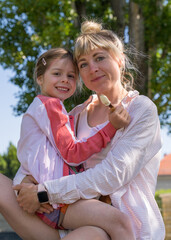 Naklejka premium Portrait of mother and daughter. A young mother tenderly hugs her little daughter. Happy, smiling girl holding ice cream in her hands. Relationships in the family, care, love of parents.