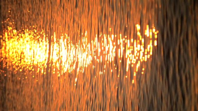 Sunny path on water surface of sea lake ocean river from shining sun during sunset dawn sunrise rising of sun dawning closeup. Waves ripples on the water. Natural background Nature backdrop Vertical