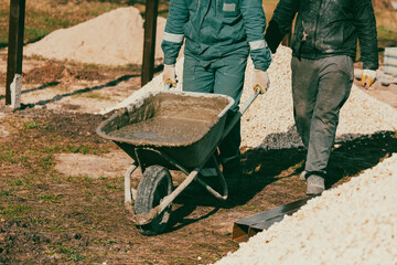 Workers are carrying a wheelbarrow with sand and cement