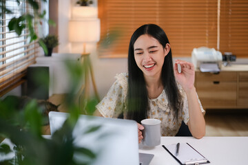 Pretty young woman talking on video call with friend or attending virtual class via laptop