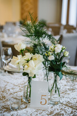 Table number 5. Stands, sign number five. Setup detail. Luxury reception. Elegant table decorated composition flowers in party area. Beautifully organized event. Wedding hall with atmospheric decor.