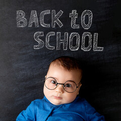 Fototapeta na wymiar A handsome little baby with glasses. Against the background of chalkboard with the inscription Back to school.