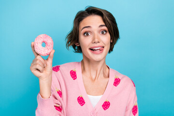Photo of cute positive lady bite tongue lick lips teeth hand hold glazed donut isolated on blue color background - obrazy, fototapety, plakaty