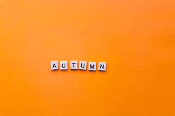 The word autumn from wooden letters on an orange background.