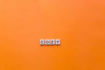 The word cozy made from wooden letters on an orange background.
