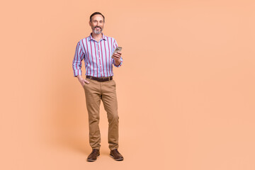 Fototapeta premium Photo of positive cheerful confident man wear striped shirt brown trousers hold smartphone read post isolated on beige color background