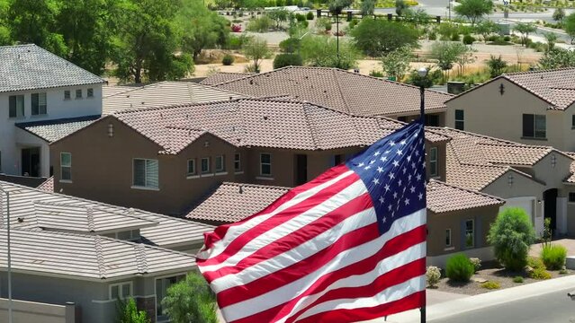 American flag waving in front of houses in housing development in Southwest USA. Aerial rising shot with zoom lens. Population growth in south theme.