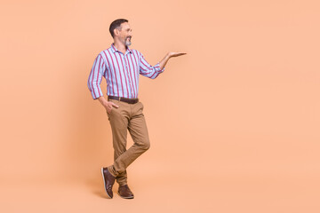 Full size photo of satisfied cheerful man wear striped shirt look at palm demonstrate offer empty space isolated on beige color background