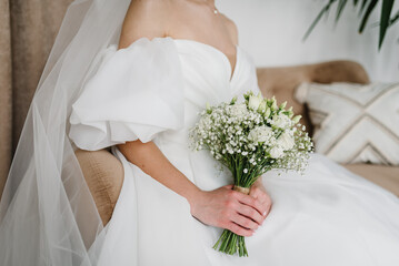 A charming bride in a stylish dress holds a beautiful bouquet of white roses and gypsophila flowers...