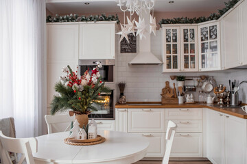 A spruce bouquet with red berries, toys, cotton on a white kitchen table. Christmas decorations in the interior. The concept of preparation for the New Year's holiday 2024.