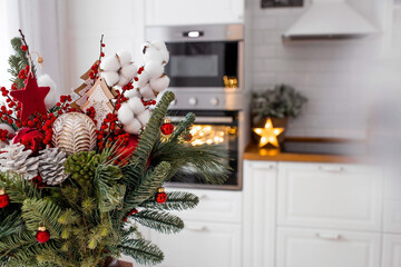 A spruce bouquet with red berries, toys, cotton on a white kitchen table. Christmas decorations in the interior. The concept of preparation for the New Year's holiday 2024.