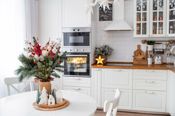 A spruce bouquet with red berries, toys, cotton on a white kitchen table. Christmas decorations in the interior. The concept of preparation for the New Year's holiday 2024.