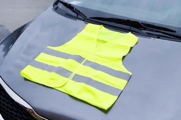 Fotobehang yellow reflective vest lies on hood of car. Safety on road in case of breakdown or stop of car © Ninaveter