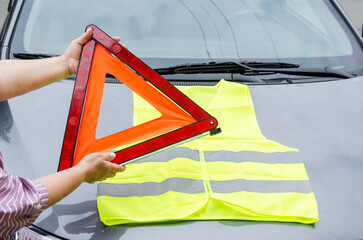 hands holding warning triangle and yellow reflective vest. Safety in case of breakdown on highway