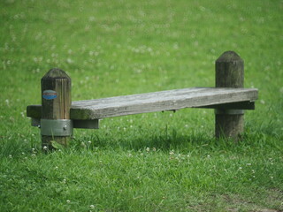 A long wooden chair with in a grassy garden. Rest seats for pedestrians that running.