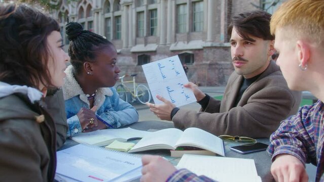 Group of young diverse economics students discussing financial graph on sheet of paper, working together on a research project or preparing for exam outdoors on campus