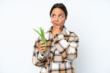 Young hispanic woman holding a green beans isolated on white background having doubts and thinking