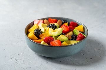 Healthy fruit salad in a grey bowl made with avocado, strawberry, raspberry, orange, blackberry and peaches. Grey background
